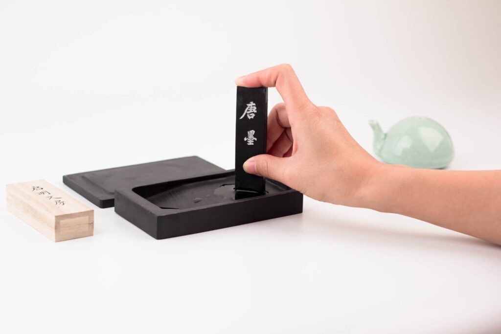 用大拇指和中指捏著墨塊，用食指頂住墨塊頂部在硯台中磨